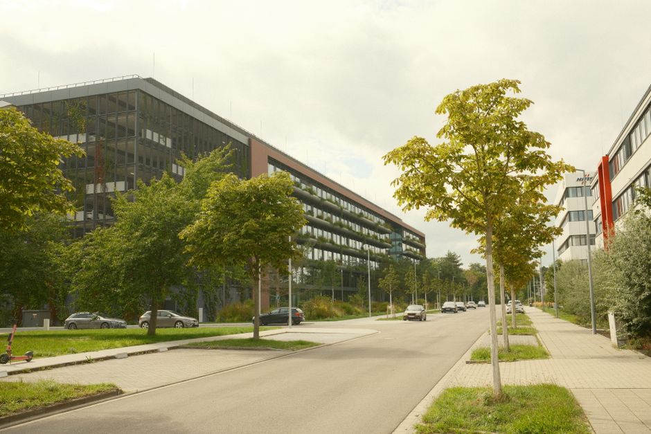 A modern urban street with office buildings and greenery on a cloudy day.
