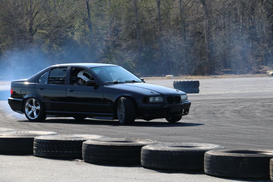 A black sedan expertly drifts on a track, surrounded by tire smoke, captured in dynamic motion.