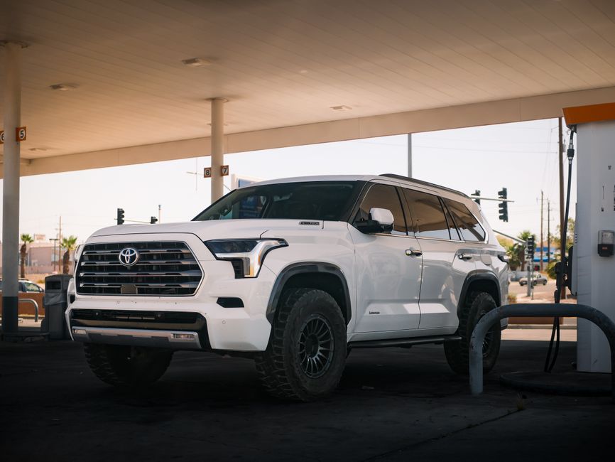 A white SUV parked at a gas station under a bright sunny day, showcasing modern automotive design.