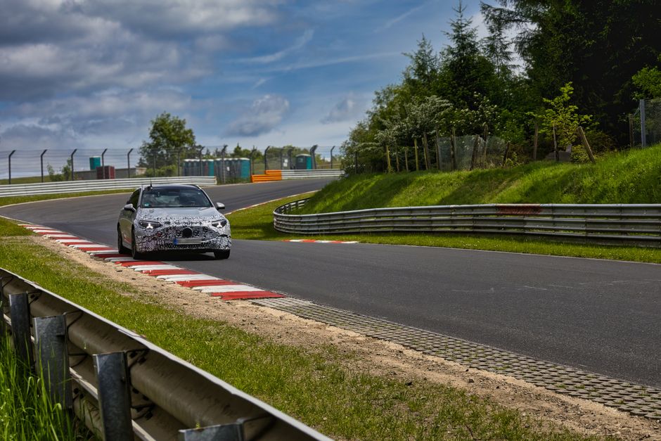 A camouflaged sports car speeds around the Nürburgring race track on a sunny day.